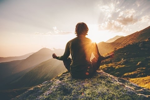 person peacefully meditating on mountain