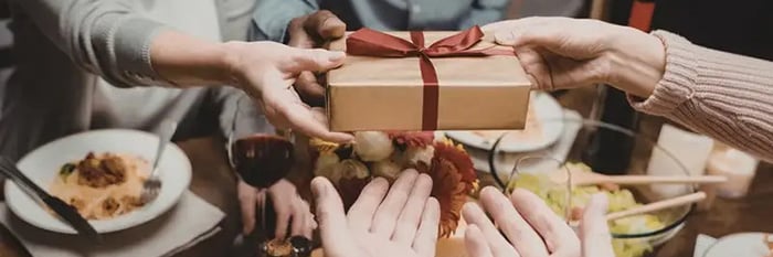 Group of friends at a holiday table extanging gifts.