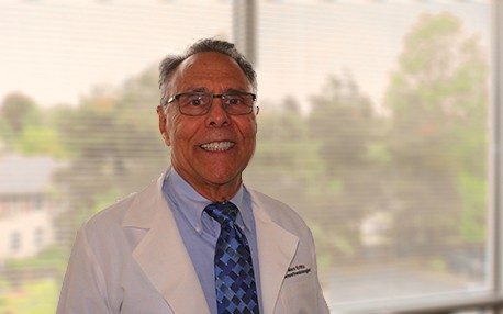 Doctor standing in front of window wearing white MD jacket.