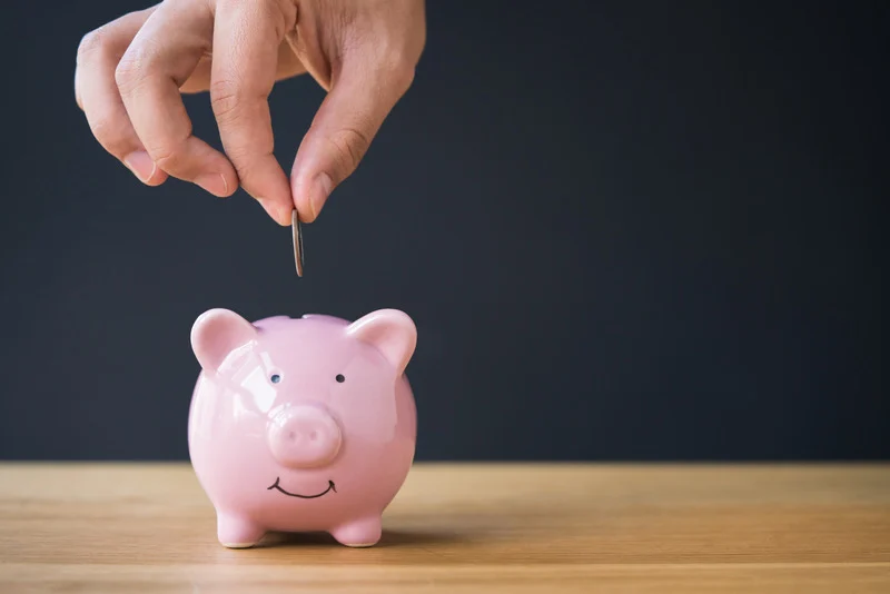 Hand dropping a coin into a piggy bank